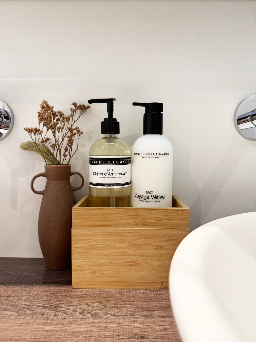 Marie-Stella-Maris hand soap and lotion in a bamboo box beside a terracotta vase of dried flowers on the vanity at Waal
