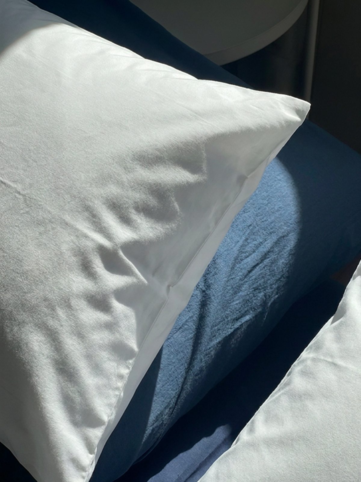 Crisp white percale bed linen at Waal in morning sunlight, layered over a deep blue throw