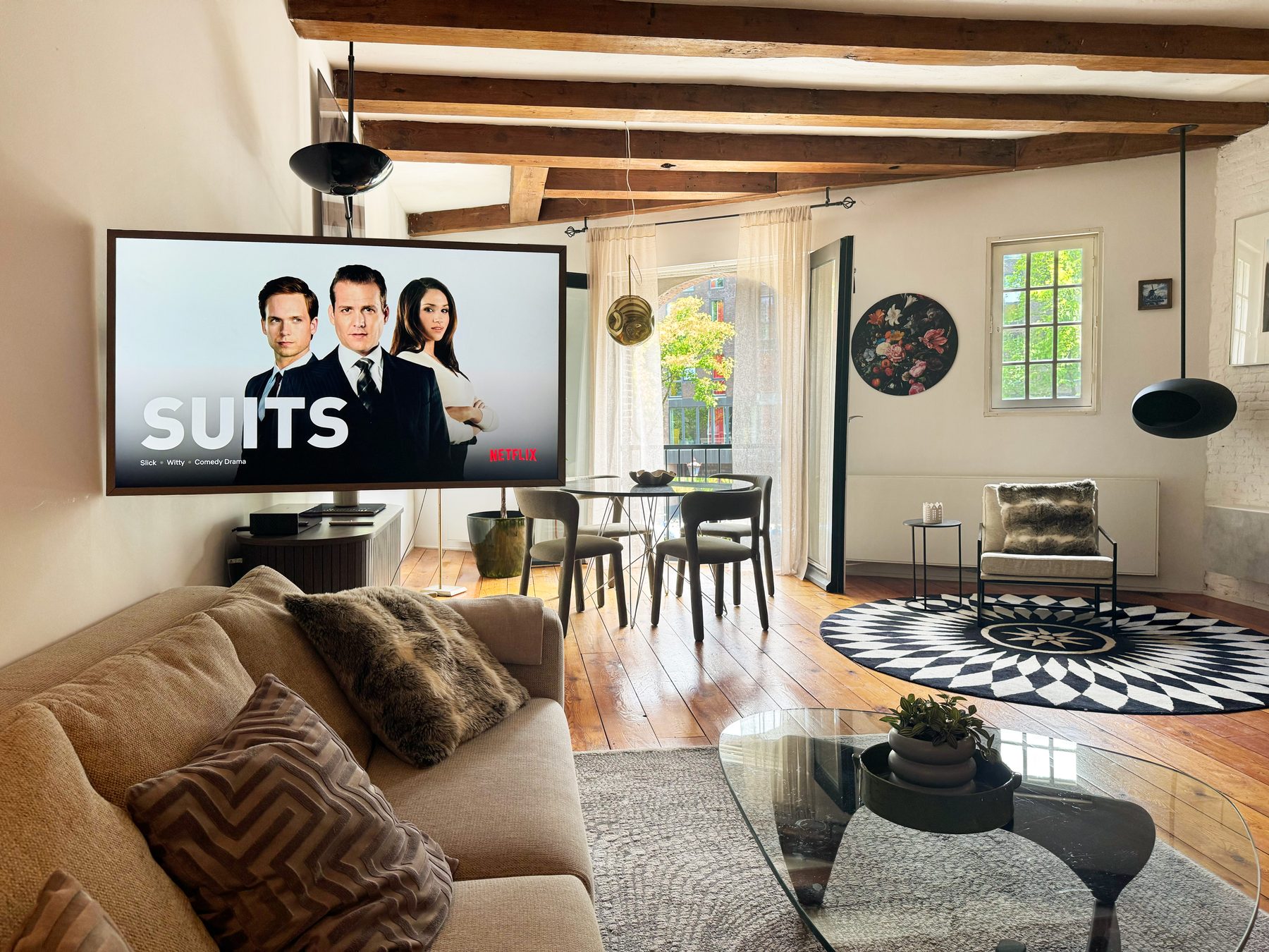 Open living area at Waal with a sectional sofa, a wall-mounted Samsung The Frame television, the dining table at the French balcony and a graphic round rug