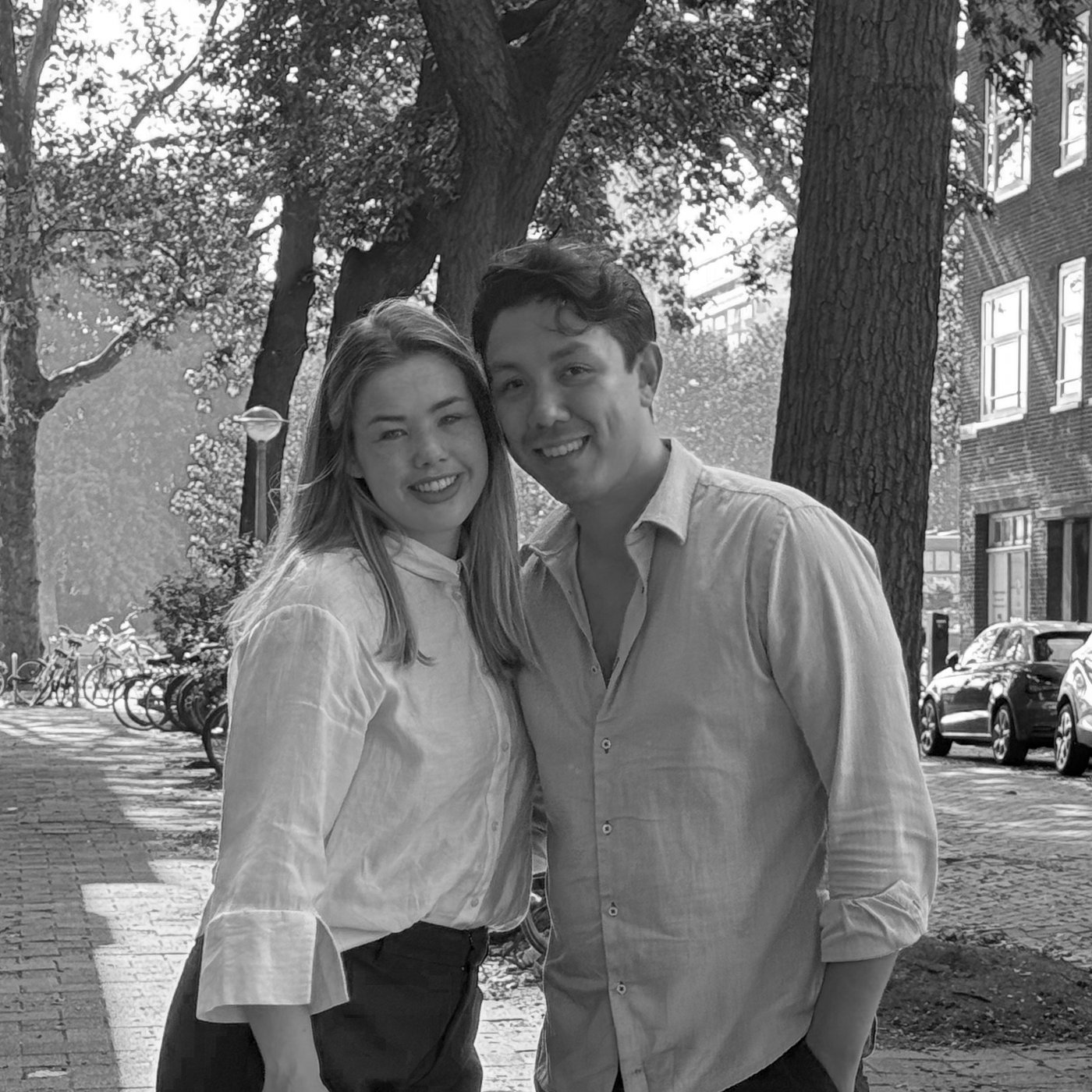 Isabelle and Vinícius, the hosts of Waal, standing together on a tree-lined Amsterdam street