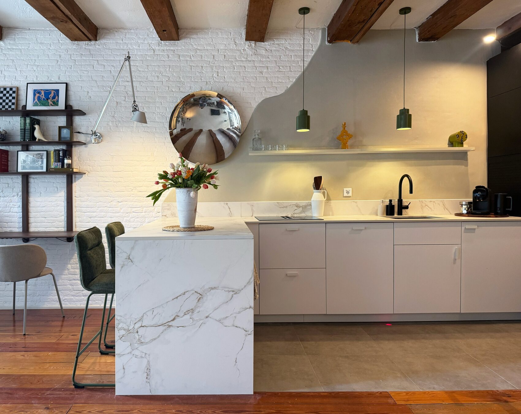 The chef's kitchen at Waal with a waterfall marble breakfast bar and green stools, induction cooktop, black tap and pendant lights under exposed beams