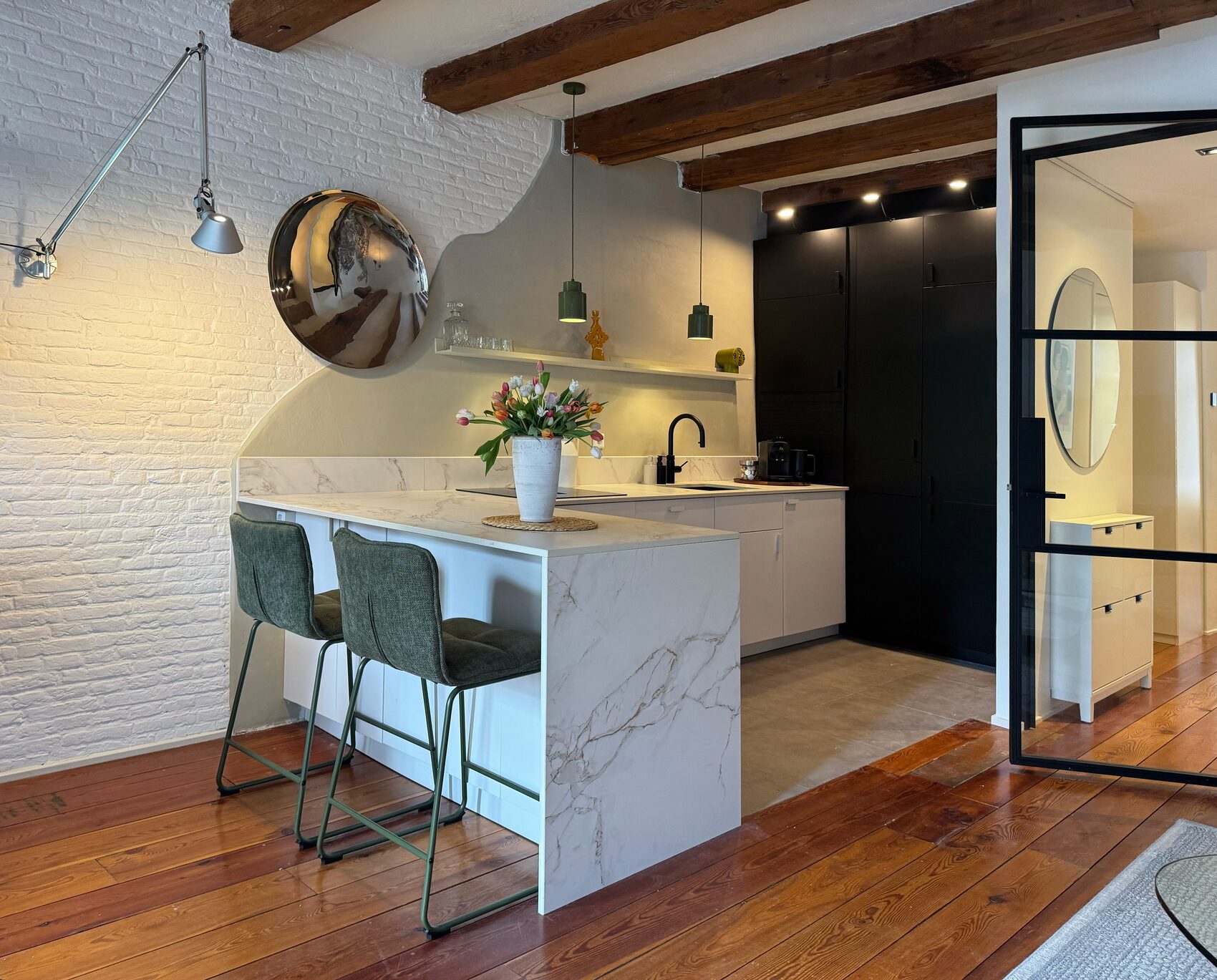 Chef's kitchen at Waal with a marble island, induction stovetop, black tap and green pendant lights against white-painted brick