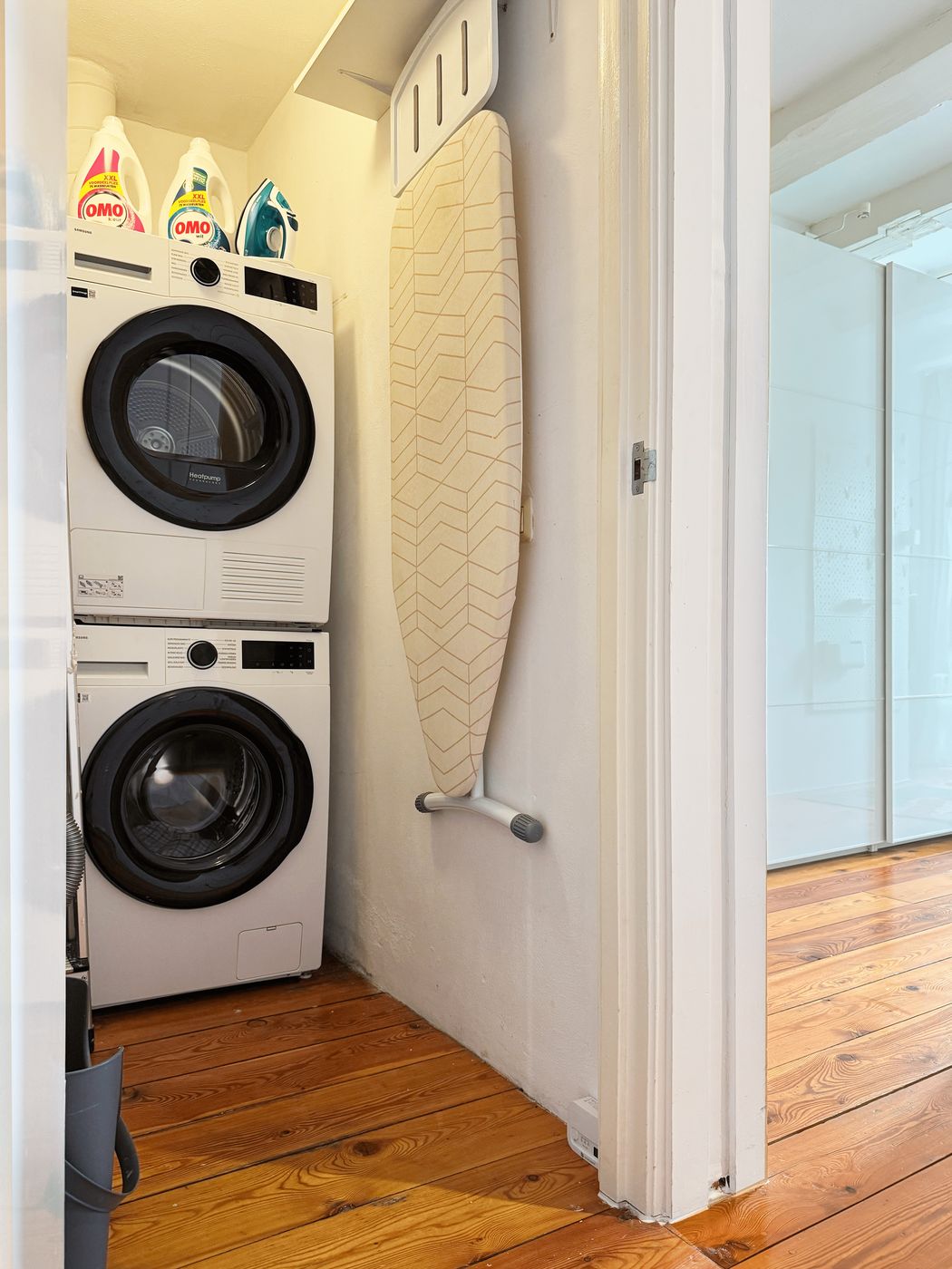 The utility nook at Waal with a stacked Samsung washer and dryer, detergent and a wall-mounted ironing board
