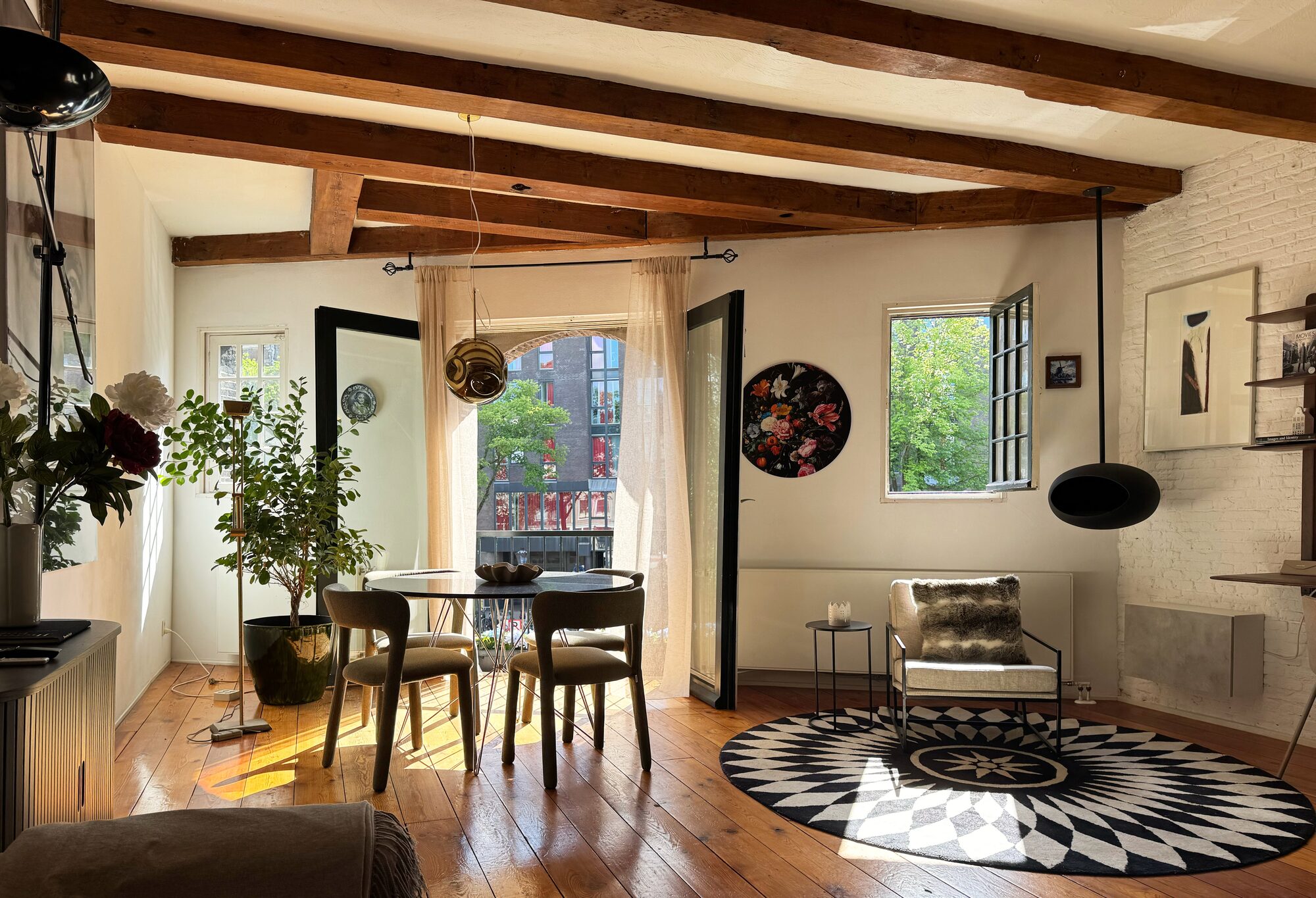 Dining table beside the French balcony at Waal, with a marble table, bouclé chairs and canal views through tall doors