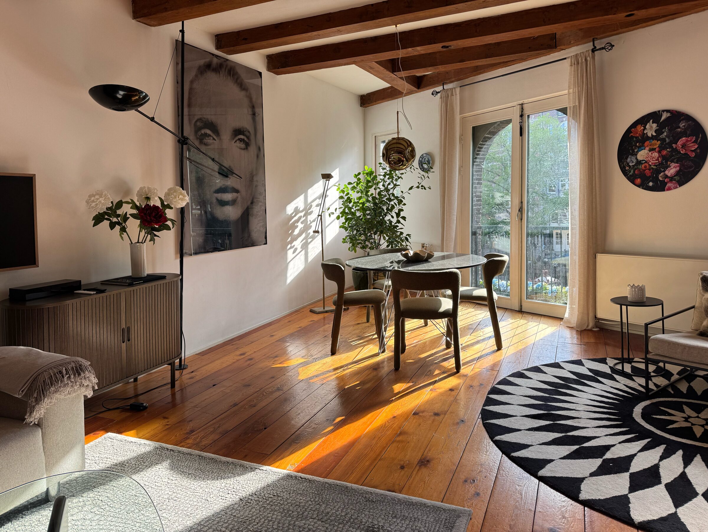 Sunlit open-plan living and dining room of Waal, with reclaimed pine floors, exposed timber beams and a French balcony over the Prinsengracht canal