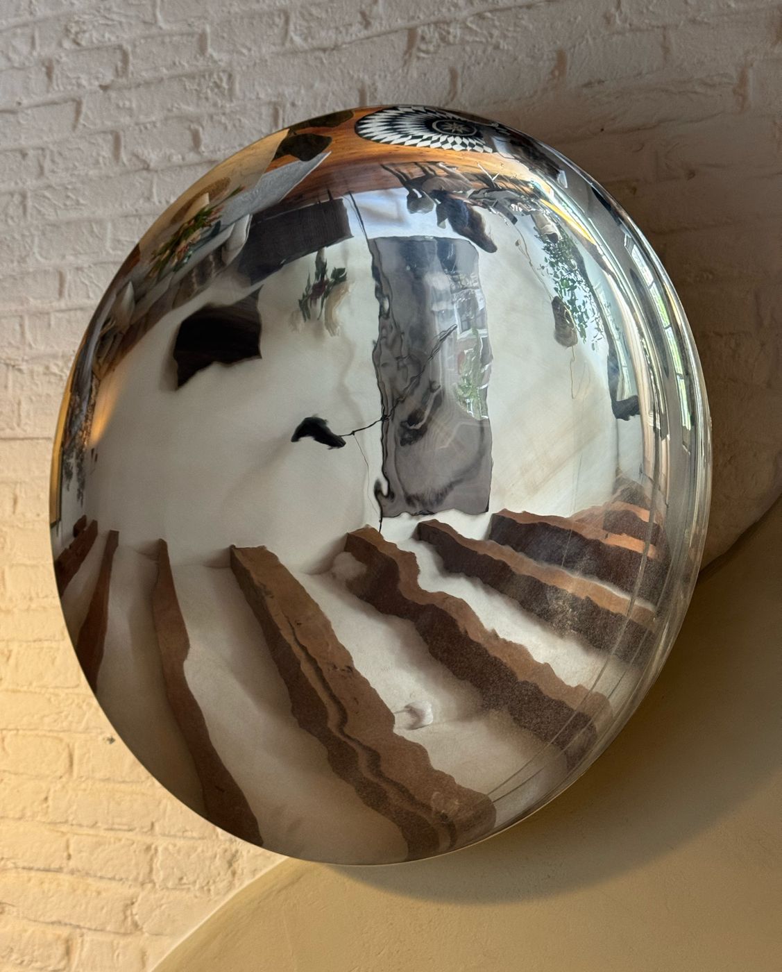 A large convex mirror at Waal reflecting the living room, exposed beams and white-painted brick