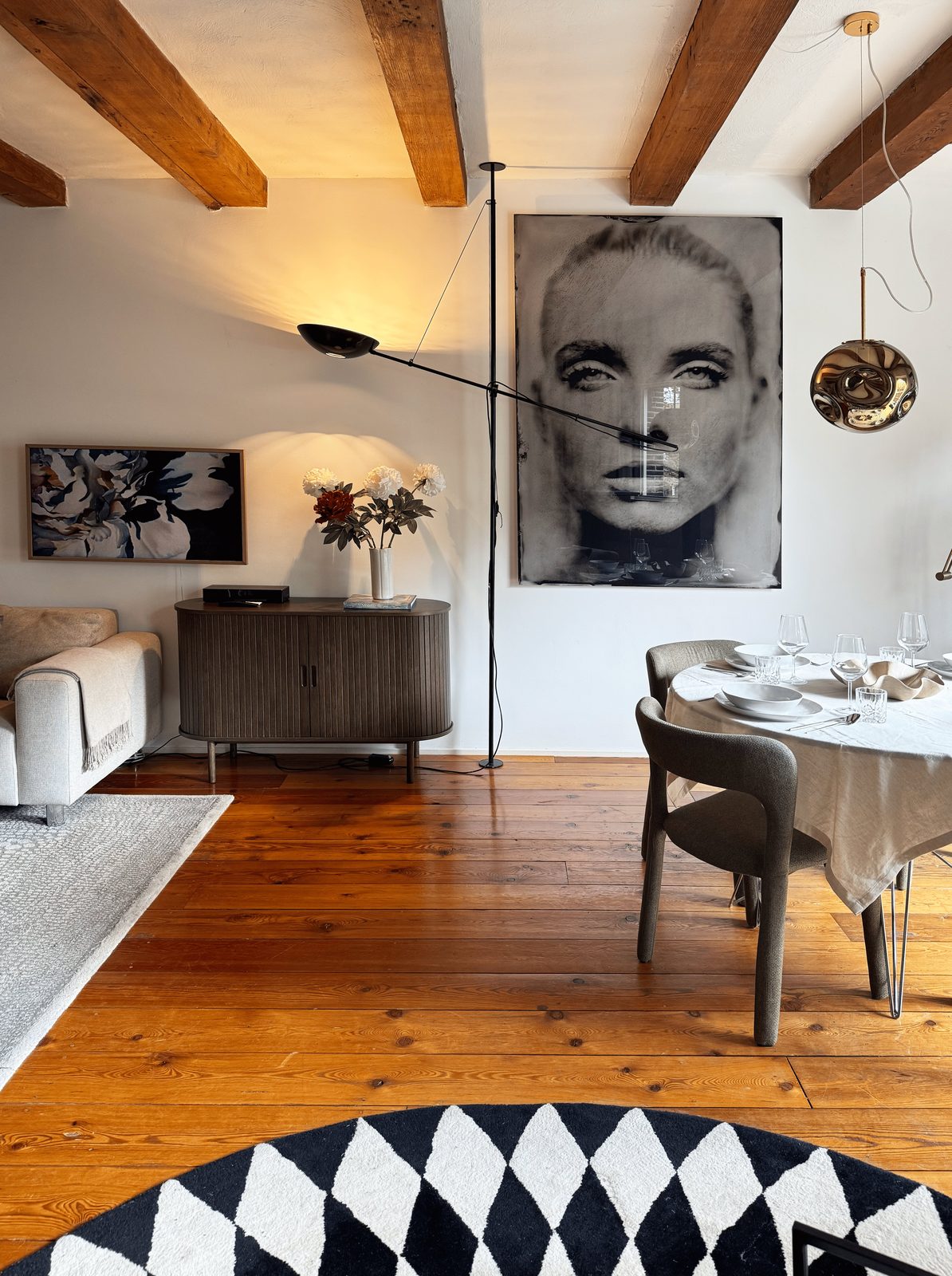 The main living and dining room of Waal in late sun, with reclaimed pine floors, a large black-and-white portrait and a fluted sideboard