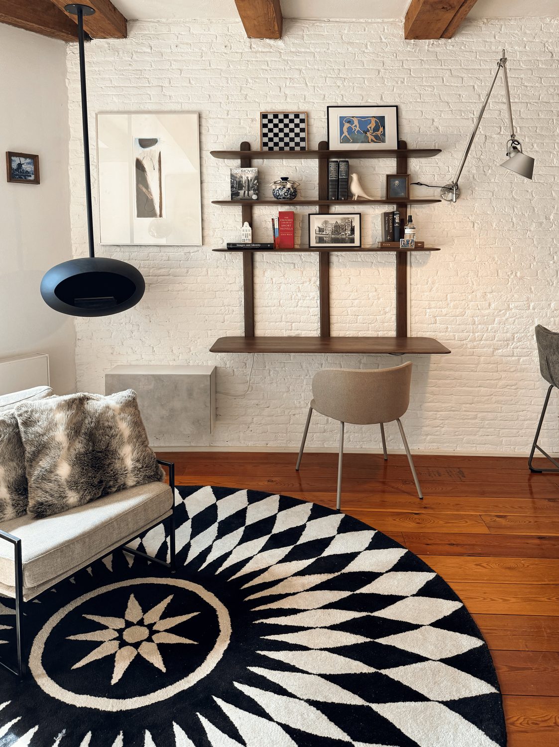 The living corner at Waal with a bespoke mangowood wall shelf and built-in desk, a suspended Le Feu fire pit and a graphic round rug
