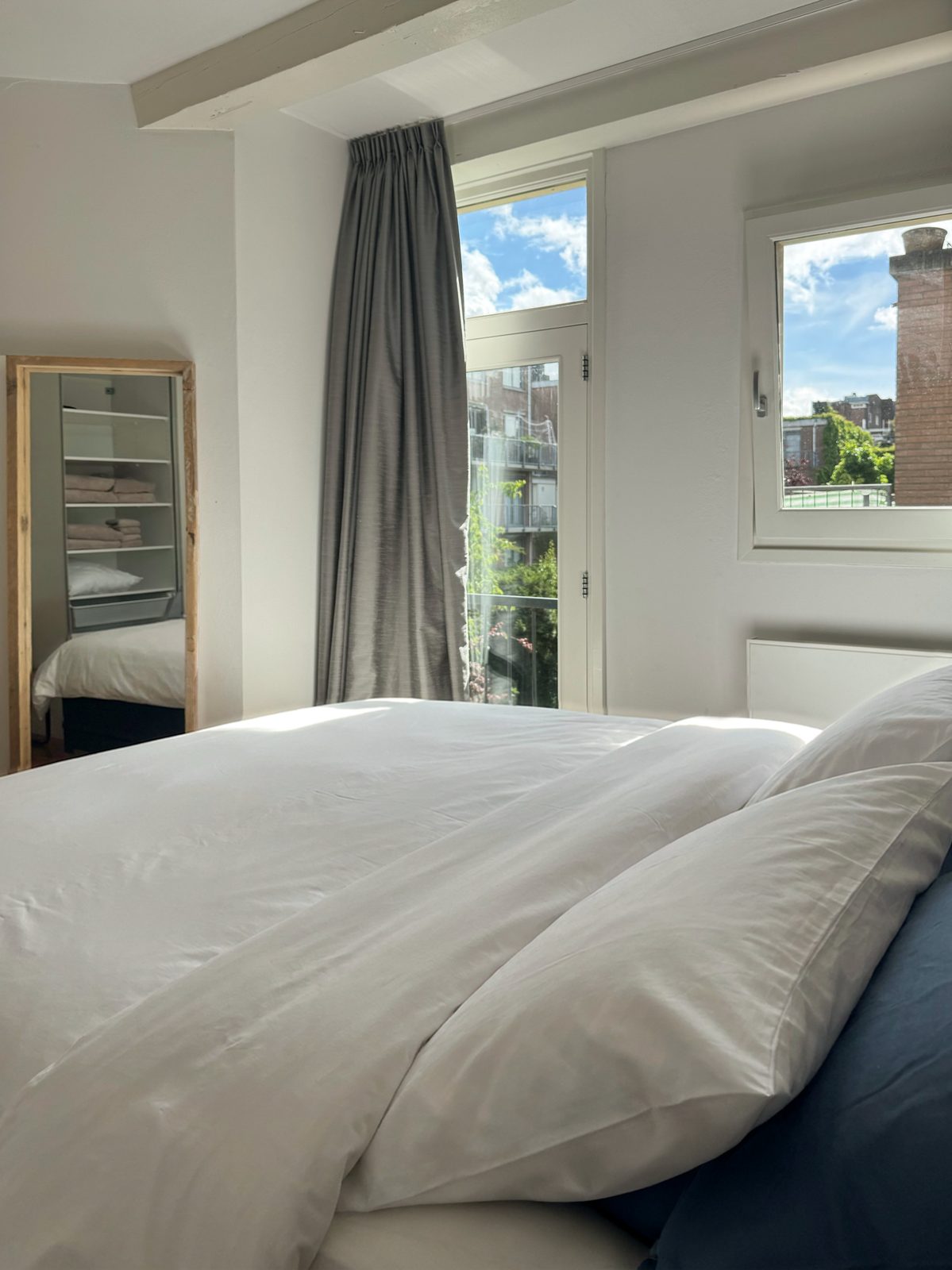 Master bedroom at Waal in bright daylight, the king bed in white percale beside a French balcony door looking onto greenery