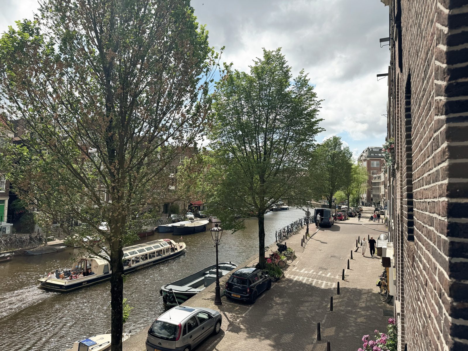 Summer view down the Prinsengracht from Waal, with a canal cruise boat passing under leafy trees and the quiet Jordaan street alongside
