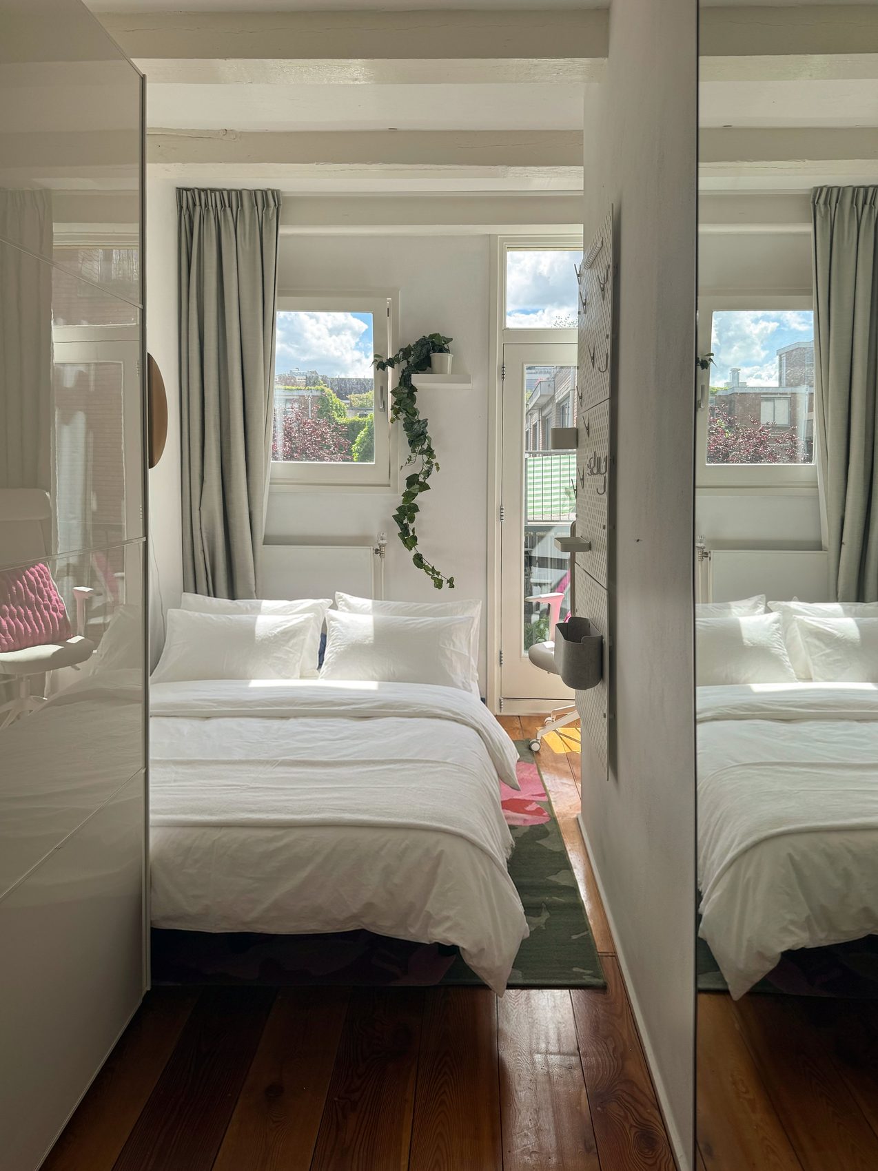 Second bedroom at Waal with a bed in crisp white linen, mirrored wardrobes, a floral rug and a window onto greenery