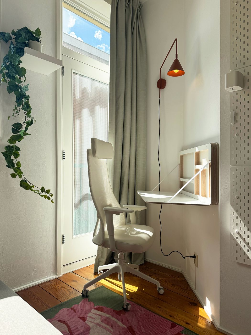 A fold-out wall desk and white ergonomic chair in the second bedroom at Waal, beside a balcony door in afternoon light