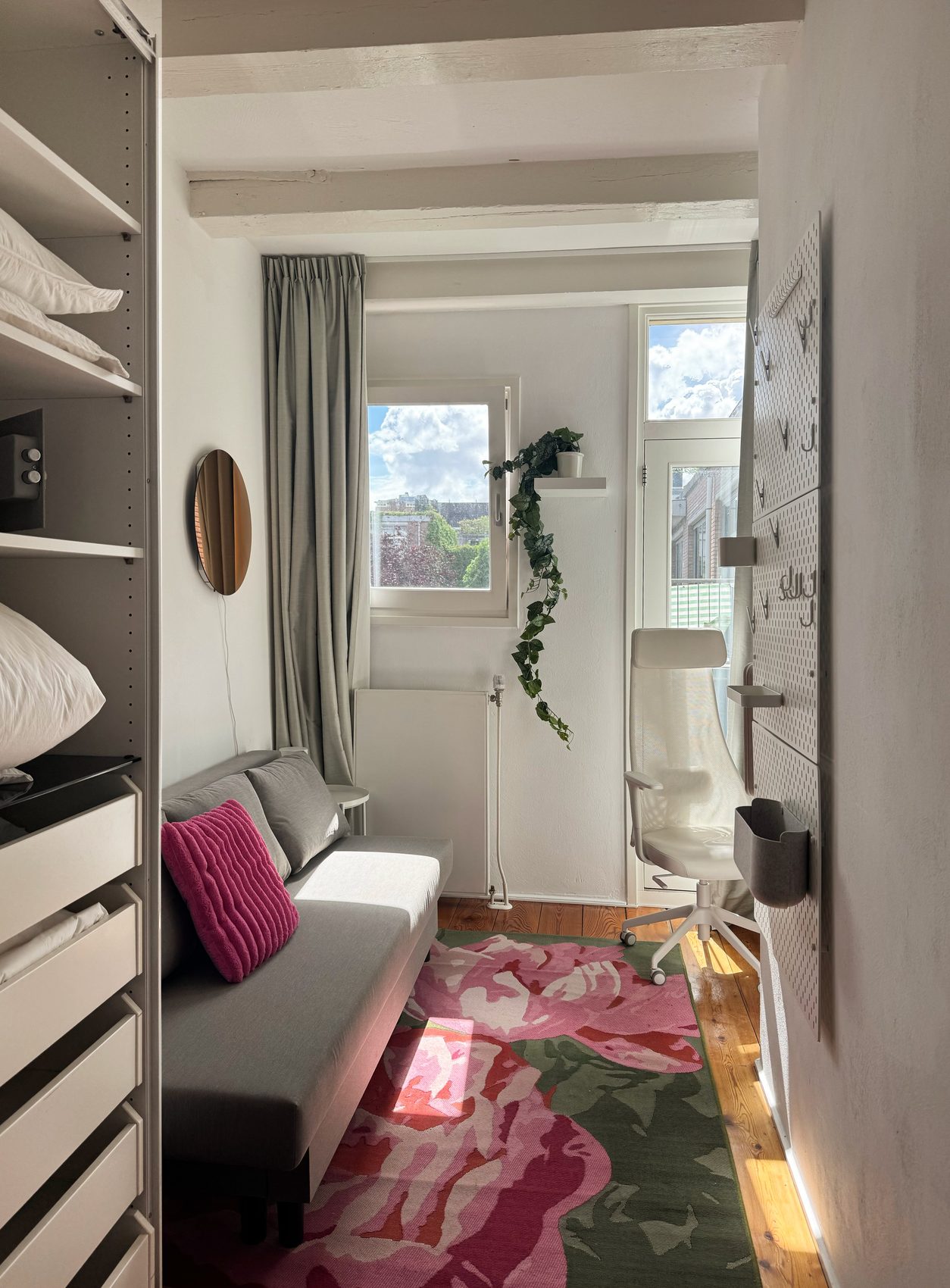 The second bedroom at Waal set up as a lounge, with a convertible sofa, a floral rug and an ergonomic chair by the window